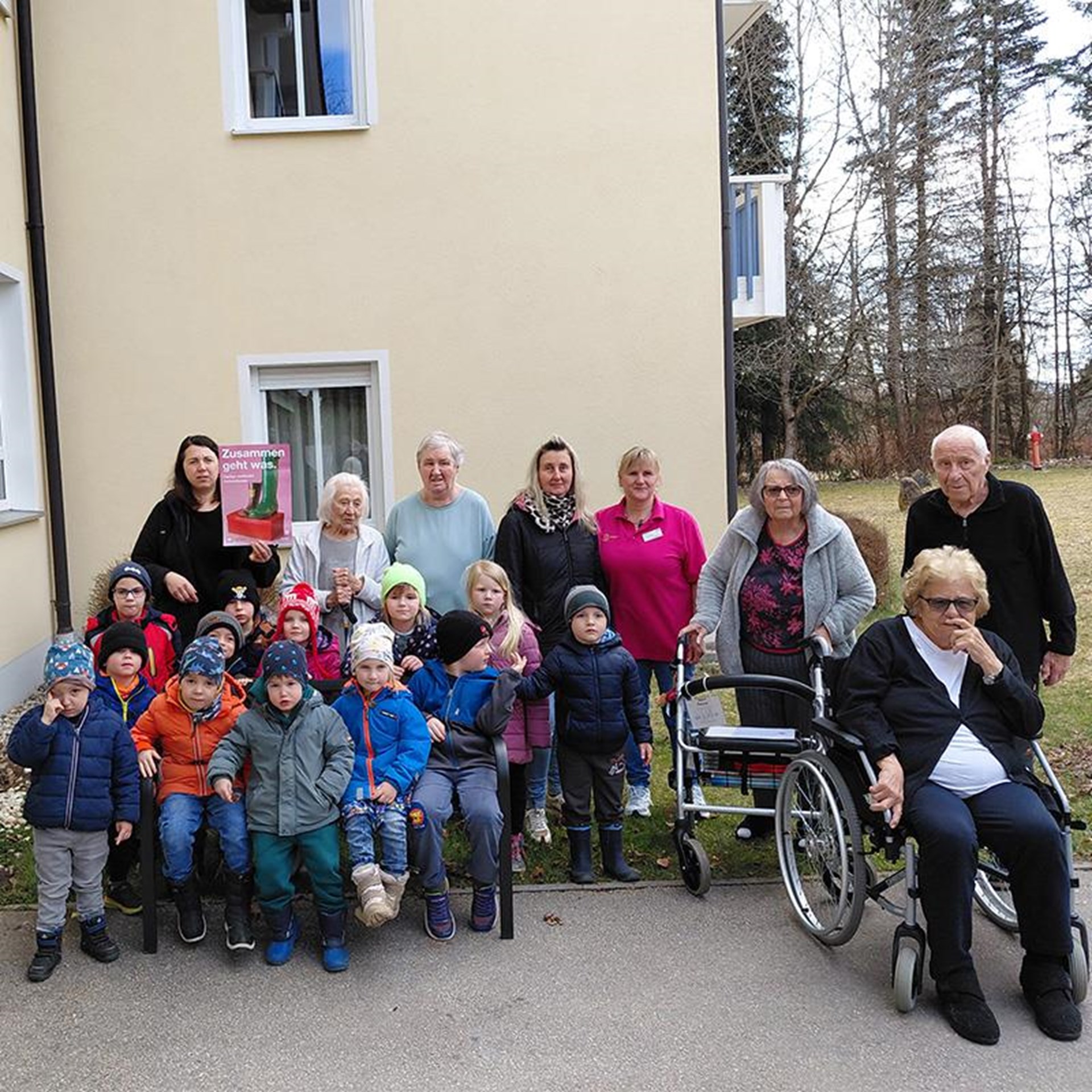auf dem Bild stehen vor einem Gebäude eine größere Gruppe Senioren und Kindergartenkinder